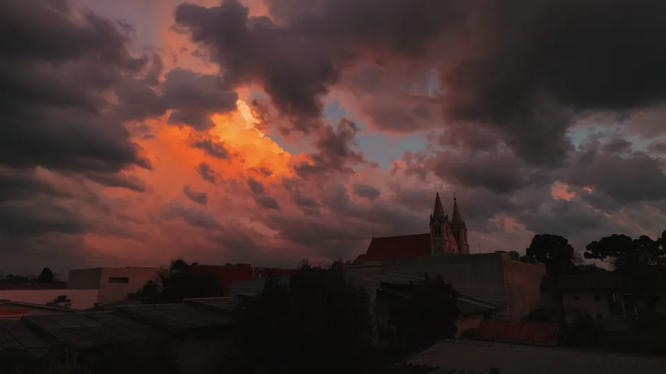 Telhados e nuvens alaranjadas no céu ao entardecer.