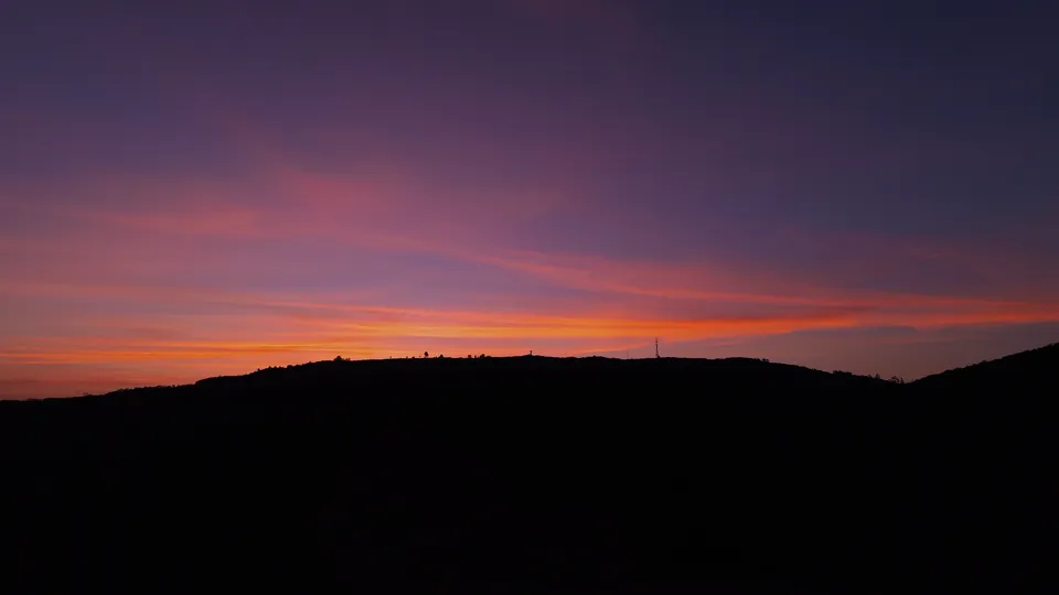 Faixas de luz rosa e laranja sobre a silhueta da paisagem.