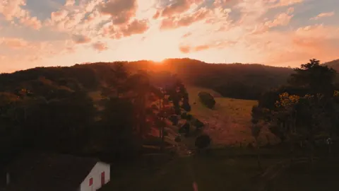O sol ilumina os campos e as árvores ao fundo da paisagem.
