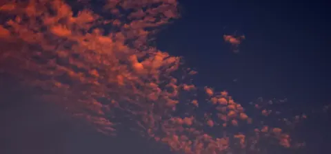 Nuvens alaranjadas contrastam com o azul do céu no entardecer.